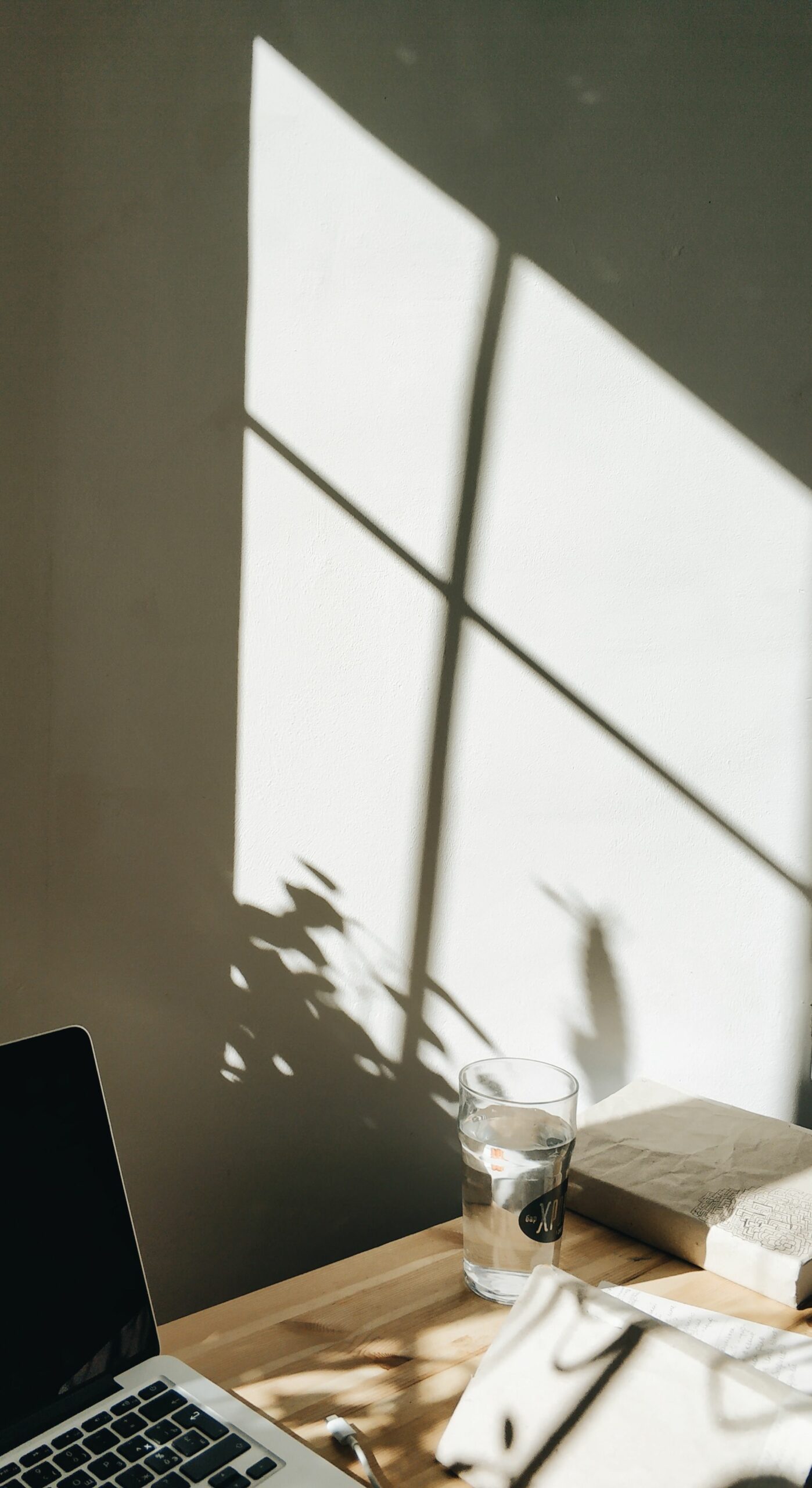 High angle shadows on wall near table with modern laptop arranged with book and water glass in cozy workspace
